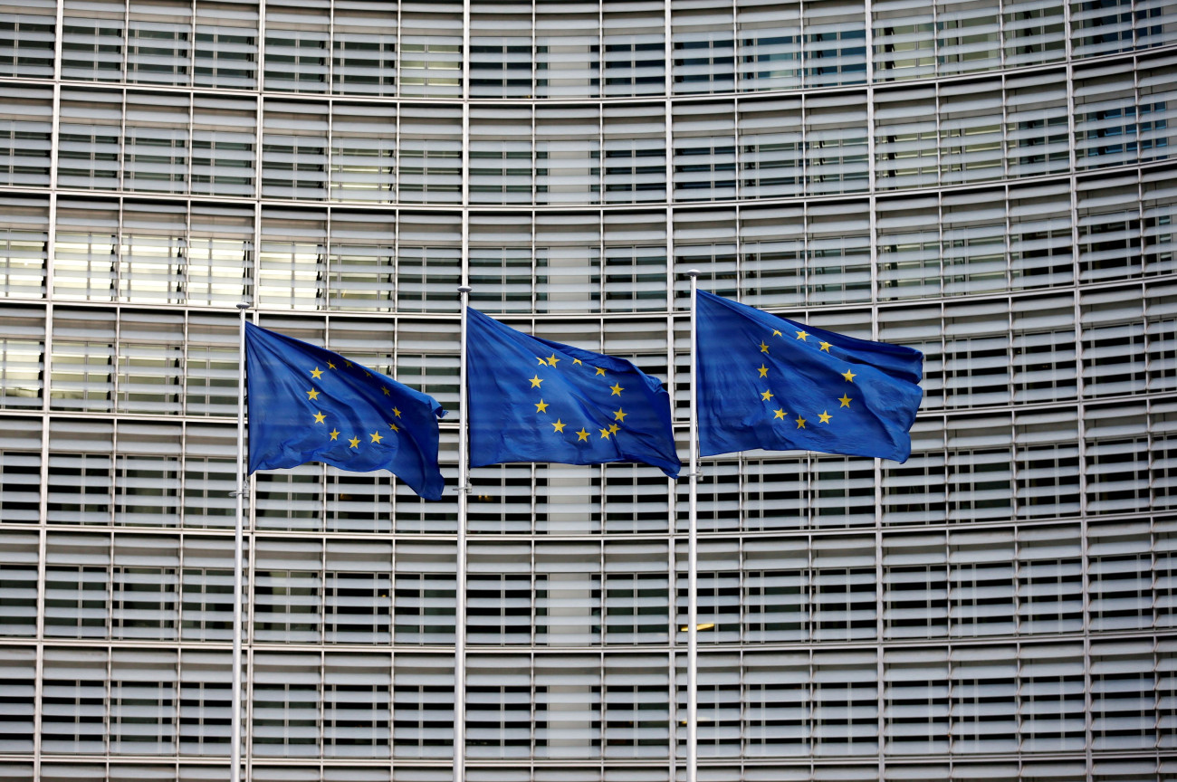 Εικόνα που δείχνει τρεις σημαίες της Ευρωπαϊκής Ένωσης μπροστά από το κτίριο της Κομισιόν στις Βρυξέλλες