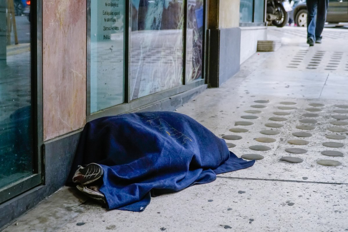 εικόνα που δείχνει άστεγο να κοιμάται στον δρόμο, σκεπασμένος με μια λεπτή κουβέρτα